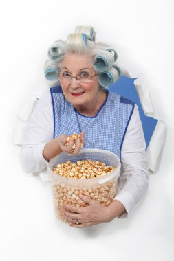 Senior woman with curlers in her hair eating popcorn clipart