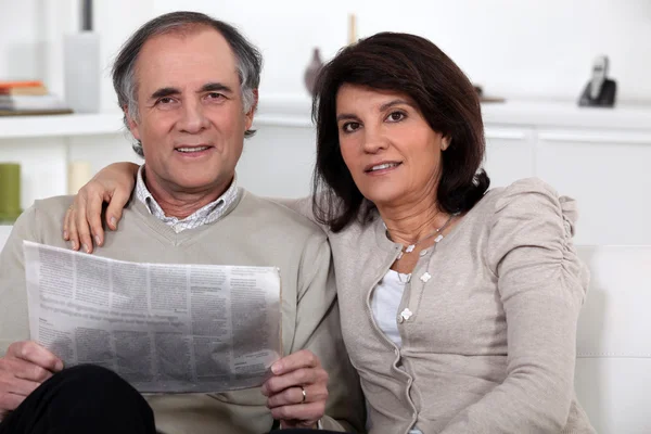 Зрелая пара, читающая газету на диване — стоковое фото