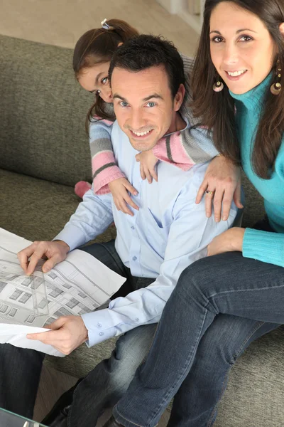 Young family relaxing on sofa with newspaper — Stock Photo, Image