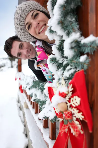 Casal inclinado para fora de um chalé de Natal — Fotografia de Stock