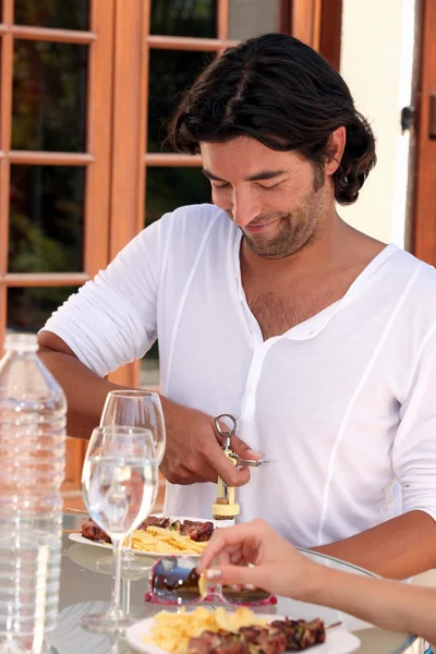 Uomo che apre una bottiglia di vino a un pranzo all'aperto — Foto Stock
