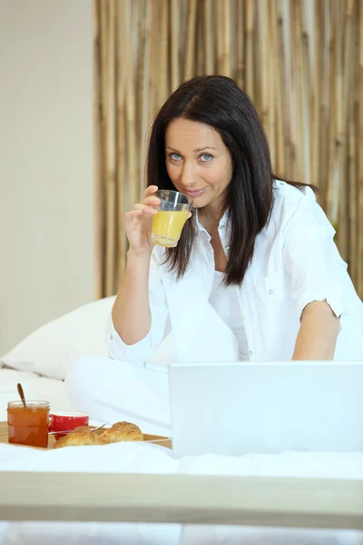 Mujer en la cama con desayuno y su portátil —  Fotos de Stock
