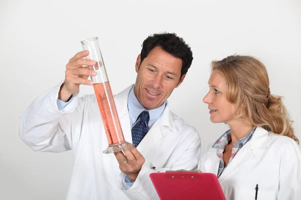 Мужчина и женщина в белых халатах с планшетом, изучают оранжевую жидкость — стоковое фото