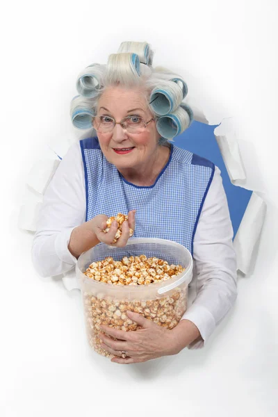 Äldre kvinna med papiljotter i håret äta popcorn — Stockfoto