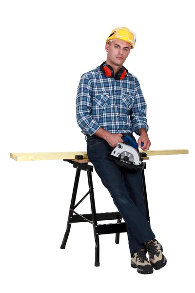 Tradesman standing in front of a workbench and holding a circular saw — Stock Photo, Image