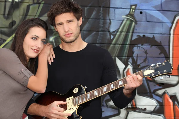 A woman and a guitarist in front of a tagged wall — Stock Photo, Image