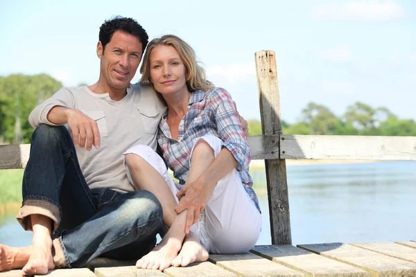 Mid age couple seated on a pontoon near a lake — Stock Photo, Image
