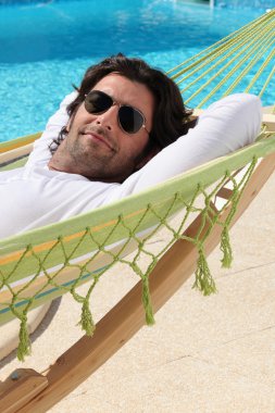 Man laid in hammock by swimming pool clipart