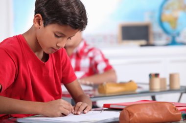 Little boy focusing on his work in classroom clipart