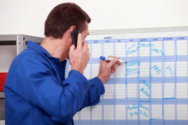 Man in blue overalls talking on the phone and writing on a board clipart