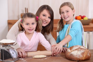 Mother rolling dough with two daughters clipart