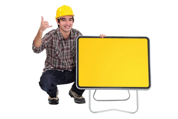 Tradesman squatting next to a traffic sign — Stock Photo, Image