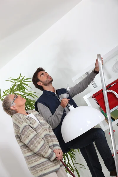 Young man putting up a light for an elderly woman — Stock Photo, Image