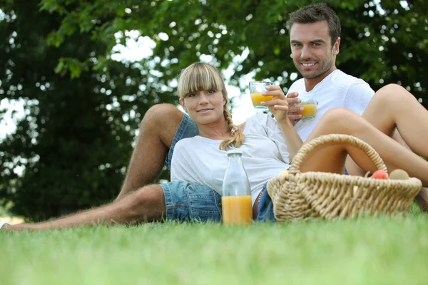 Casal beber suco de laranja em um parque — Fotografia de Stock
