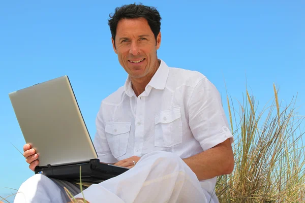 Чоловік посміхається на пляжі з ноутбуком . — стокове фото