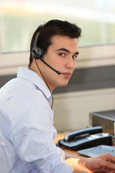 Genç adam bir bilgisayar önünde bir kulaklık takıyor — Stok fotoğraf