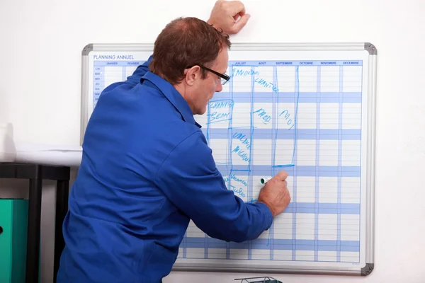 Construction worker writing in deadlines on a calender — Stock Photo, Image