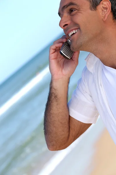 Uomo sorridente su un telefono cellulare sulla spiaggia — Foto Stock