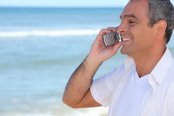 Hombre sonriente usando un celular junto al océano — Foto de Stock