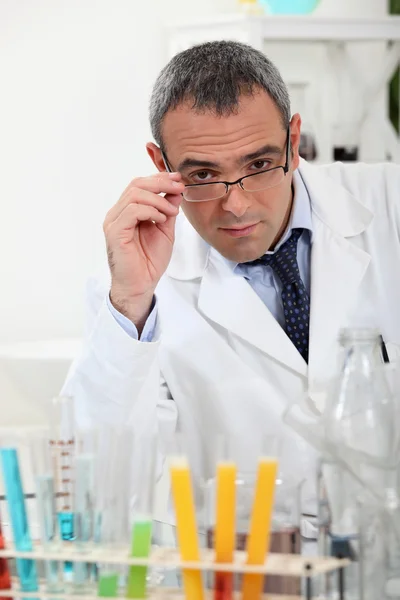 Scientist touching his glasses behind test tubes in a laboratory — Stock Photo, Image