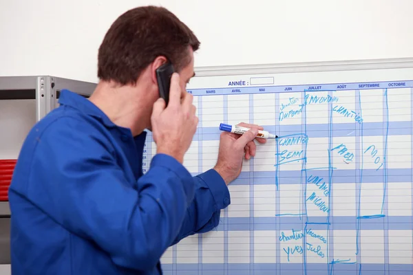 Man in blauwe overalls praten aan de telefoon en schrijven op een bord — Stockfoto