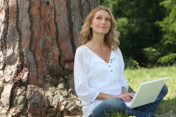 Jovem mulher sentou-se à árvore com laptop — Fotografia de Stock