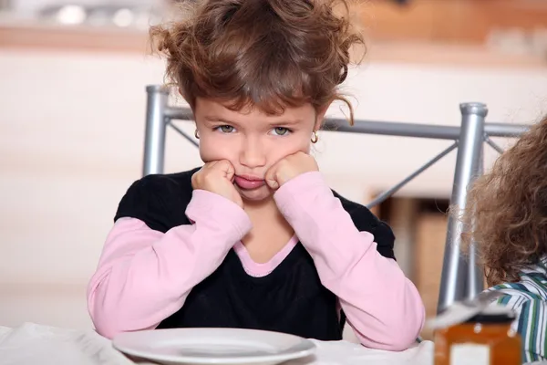 Sulky flicka sitter vid frukostbordet — Stockfoto