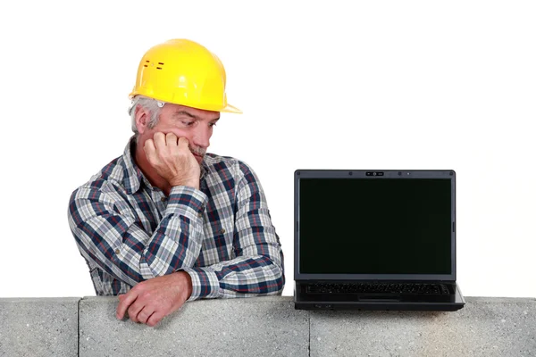 Запутавшийся строитель средних лет смотрит на ноутбук Стоковое Фото