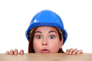 Female builder peering over ledge clipart