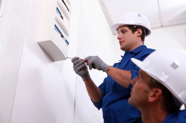 Electricians fitting a fuse box clipart