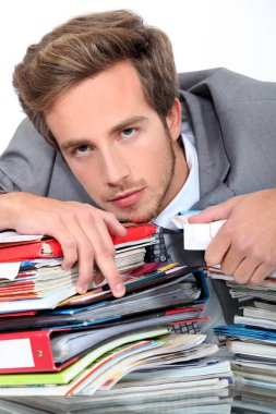 Young man lying down on a desk full of binders and notebooks clipart