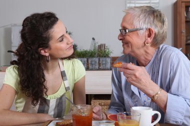 Elderly dame and young brunette having breakfast clipart