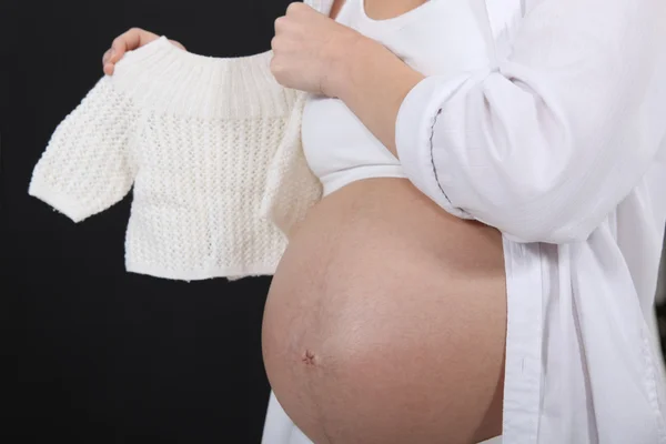 Беременная женщина держит свитер ребенка — стоковое фото
