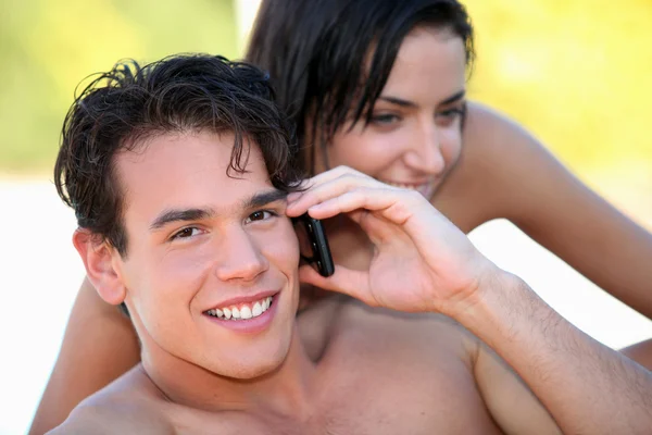 Knappe jonge man spreken op zijn mobiele telefoon op het strand — Stockfoto