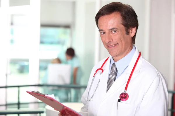 Male doctor holding red clipboard — Stock Photo, Image