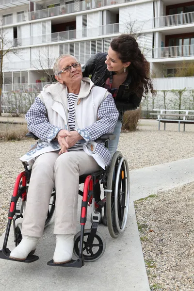 Junge Frau schubst eine ältere Frau im Rollstuhl — Stockfoto