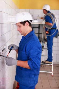 Couple of electricians wiring a building clipart