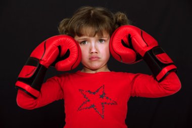 Little girl with boxing gloves pulling a face against black background clipart