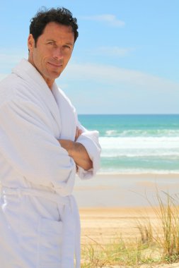 Man in a bathrobe standing on a sandy beach clipart