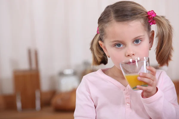Ένα κοριτσάκι πίνουν χυμό πορτοκαλιού στην κουζίνα. — Φωτογραφία Αρχείου