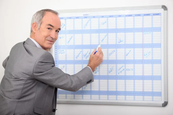 Uomo d'affari più anziano che scrive su un wall planner — Foto Stock