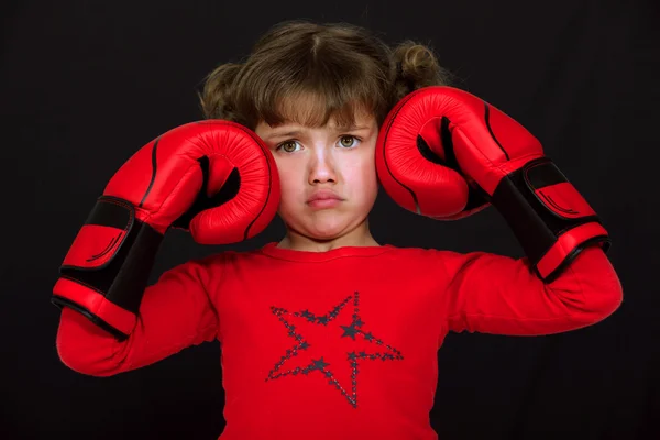 stock image Little girl with boxing gloves pulling a face against black background