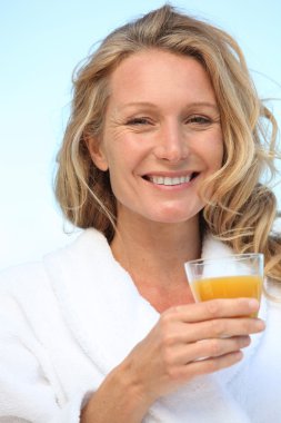 A woman wearing a dressing gown and drinking orange juice. clipart