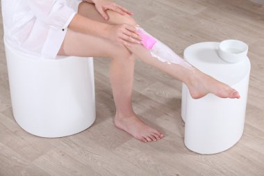 Woman putting hair removal on her leg clipart