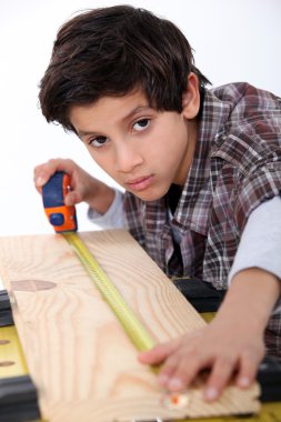 Young boy measuring a plank of wood clipart