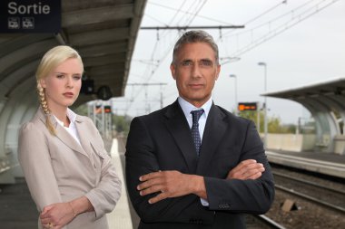 A blonde woman and a mature man well dressed in a train station clipart