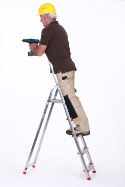 Tradesman standing on a stepladder and using a power tool clipart