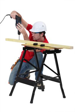 Handyman drilling a piece of wood. clipart