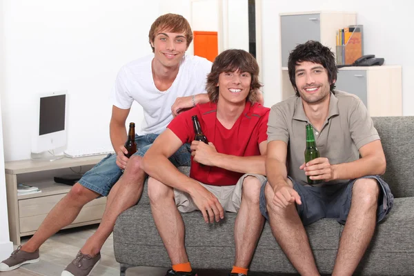 Τρεις άνδρες που κάθισε στον καναπέ, κρατώντας μπουκάλια μπύρας — Φωτογραφία Αρχείου