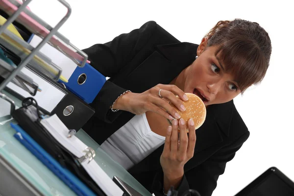 Kobieta jedzenie hamburgera na biurko — Zdjęcie stockowe
